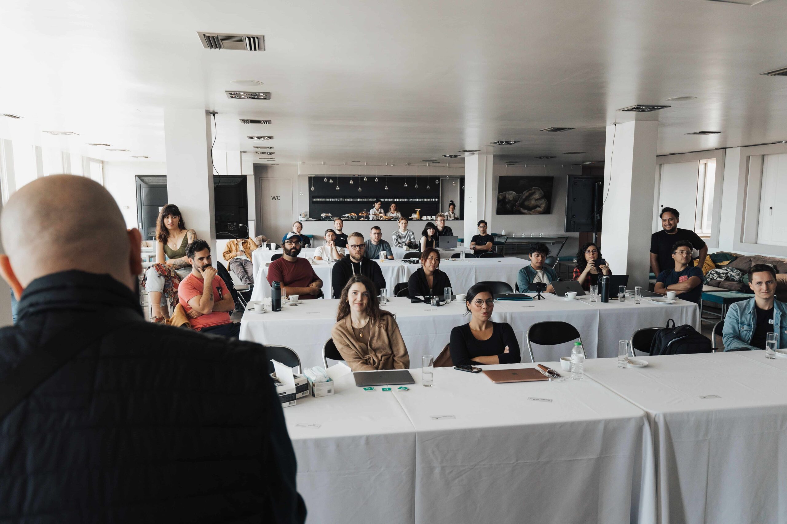 A speaker addresses an audience seated at tables.